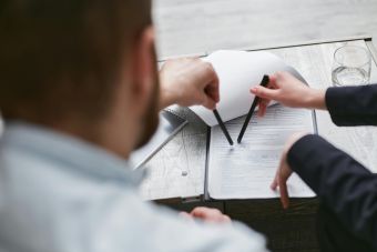 Two individuals analyzing a business contract with pens on a wooden surface.